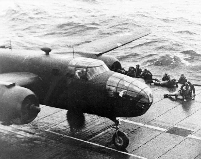 With flight deck personnel dropping to the deck to avoid its turning propellers, A north American B-25B Mitchell medium bomber starts its takeoff roll aboard USS Hornet (CV-8), 18 April 1942. (U.S. Navy)