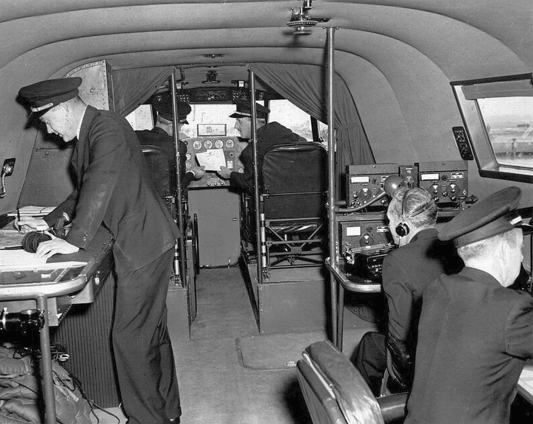 The flight deck of a Boeing 314. At the left, standing, is the airliner's navigator. Beyond him are the captain (left) and co-pilot. On the right side of the cabin are the radio operator and flight engineer. (Unattributed) 