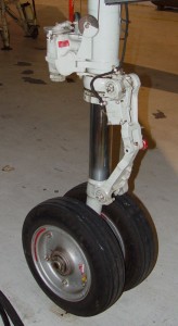 This photograph shows the lower section of the nose gear strut of an F-100 Super Sabre. The scissors ling is the hinged assembly. A red pin is visible at teh center hinge. Thi spin had been removed by ground handlers to tow the fighter, but had not been reinstalled before Lt. Brooks' flight.