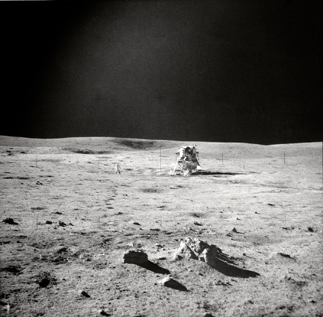 Astronaut Edgar D. Mitchell, lunar module pilot, photographed this sweeping view showing fellow Moon-explorer astronaut Alan B. Shepard Jr., mission commander, and the Apollo 14 Lunar Module (LM). A small cluster of rocks and a few prints made by the lunar overshoes of Mitchell are in the foreground. Mitchell was standing in the boulder field, located just north by northwest of the LM, when he took this picture during the second Apollo 14 extravehicular activity (EVA-2), on February 6, 1971. (Edgar D. Mitchell/NASA)