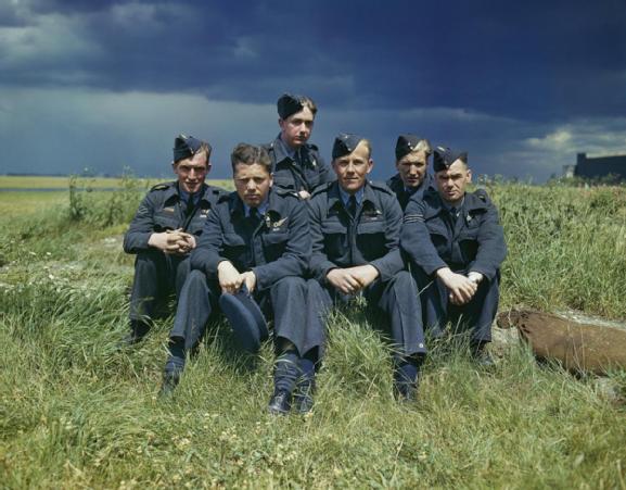 The crew of Lancaster ED285/`AJ-T' sitting on the grass, posed under stormy clouds. Left to right: Sergeant G Johnson; Pilot Officer D A MacLean, navigator; Flight Lieutenant J C McCarthy, pilot; Sergeant L Eaton, gunner. In the rear are Sergeant R Batson, gunner; and Sergeant W G Ratcliffe, engineer. Flight Lieutenant Joe McCarthy (fourth from left) and his crew of No. 617 Squadron (The Dambusters) at RAF Scampton, 22 July 1943.