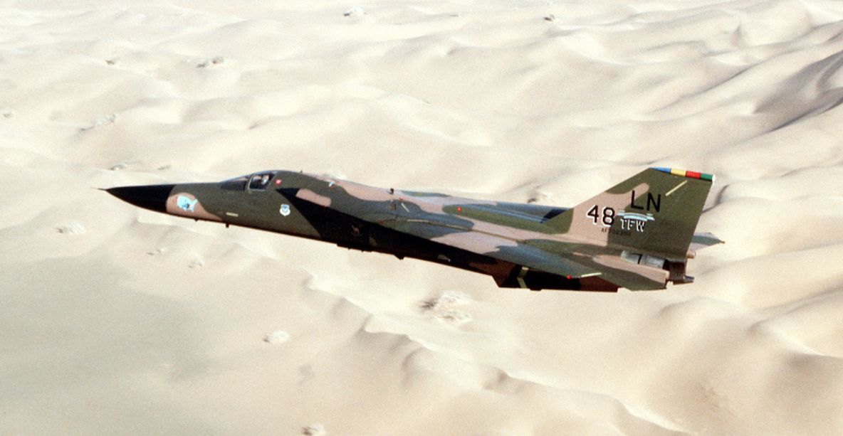 General Dynamics F-111F 70-2380, 48th Tactical Fighter Wing, with wings swept for high-speed flight, over a desert landscape. (U.S. Air Force)