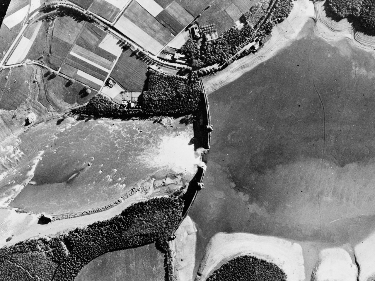 Post-strike reconnaissance photograph shows the breach of the Mohne Dam in the Ruhr Valley, 16 May 1943. (Imperial War Museum)