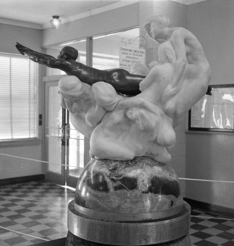 The Blériot Trophy, photographed 12 June 1961. "Side view of The Blériot Trophy on display. It is the figure of a naked man made of black marble in a flying position emerging from clouds. The clouds are white stone and are the figures of women in various poses on top of a marble dome." (University of North Texas Libraries)