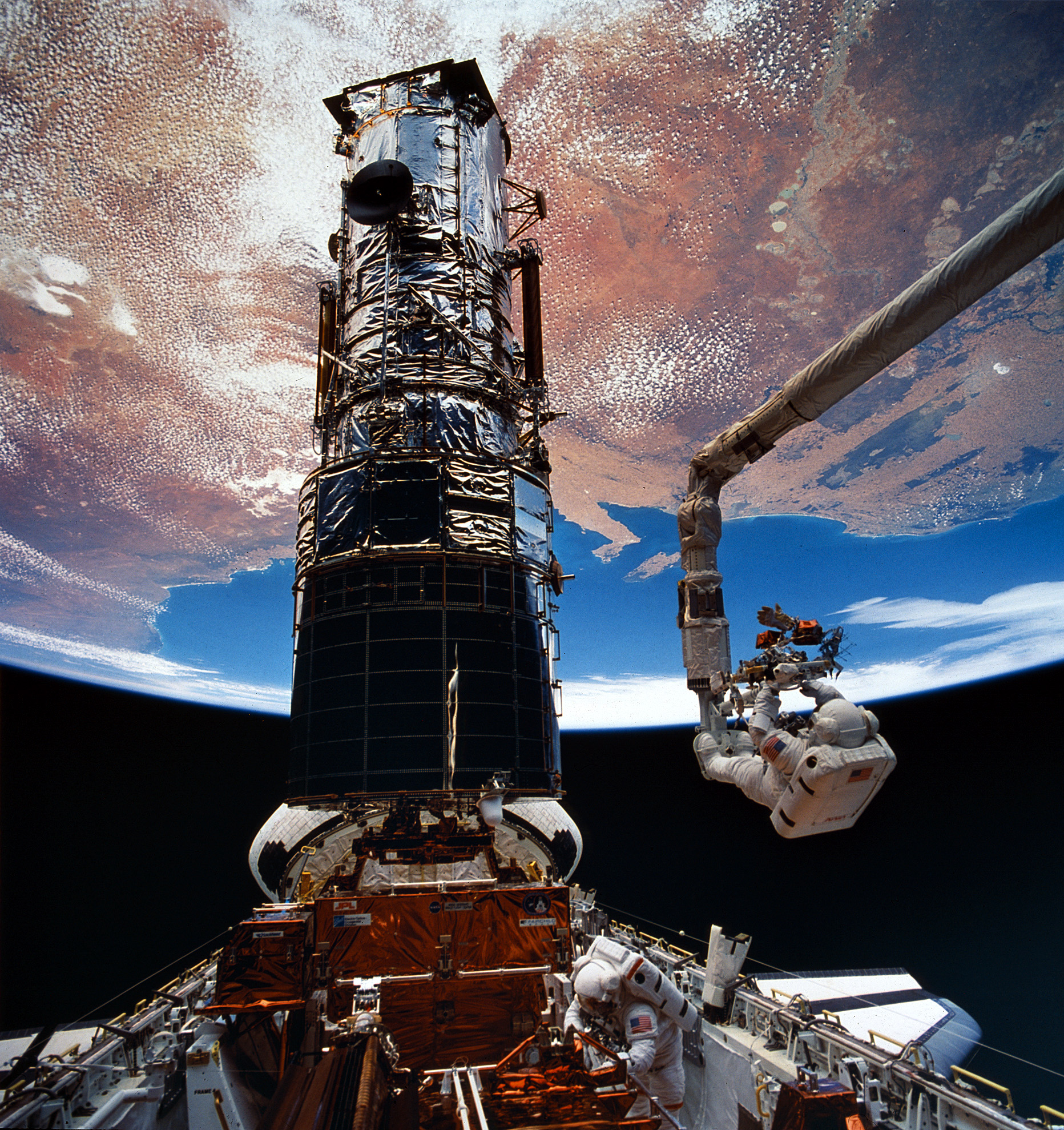 Mission Specialists Jeffrey A. Hoffman (bottom, right of center) and Story Musgrave, on the manipulator arm, with the Hubble Space telescope during EVA 5. (NASA) 