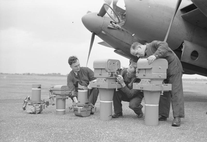 "Instrument workers line up aerial cameras at Benson, Oxfordshire, before installing them in a De Havilland Mosquito PR Mark IX: (left to right) two Type F.24 (14-inch lens) vertical cameras, one F.24 (14-inch lens) oblique camera, two Type F.52 (36-inch lens) 'split pair' vertical cameras." (Imperial War Museum CH-18399)
