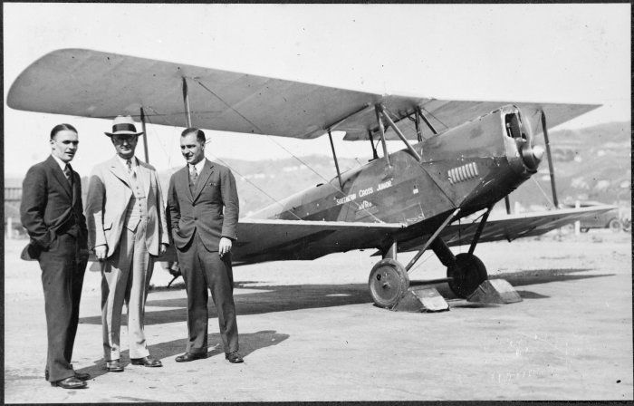Photograph of Guy Menzies and two other men standing beside his Avro Avian biplane "Southern Cross Junior" at an unidentified aerodrome (probably Wellington), taken in 1931 by Sydney Charles Smith.
