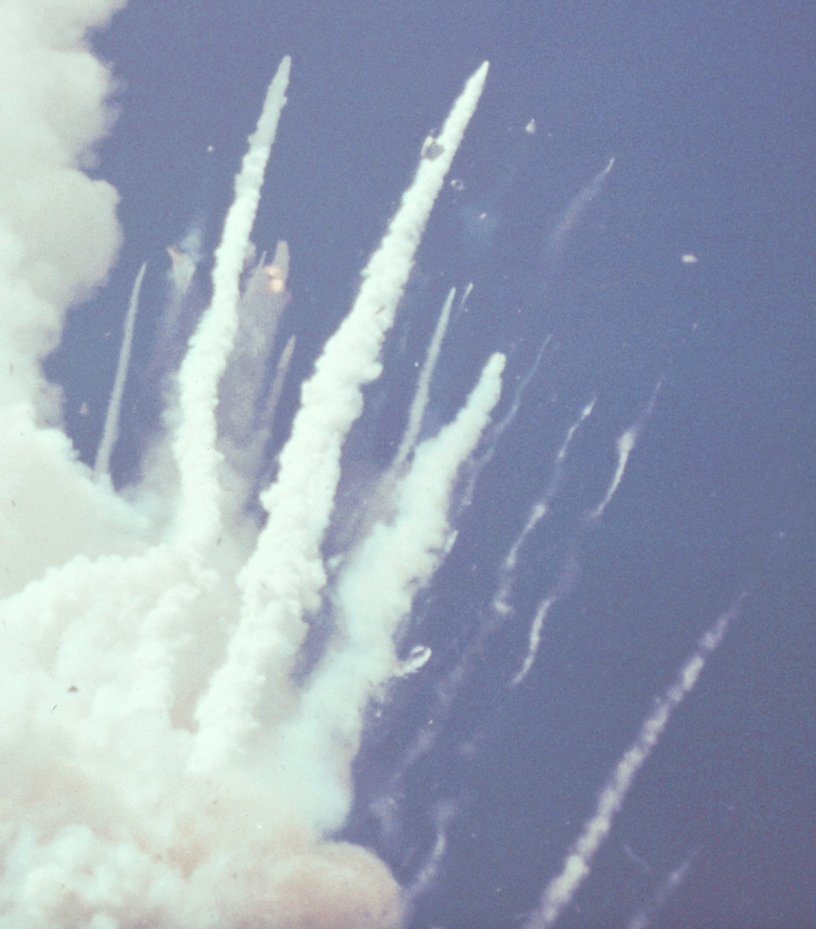 The crew cabin of Space Shuttle Challenger is visible near the end of the smoke plume at the upper center of this photograph, still climbing at supersonic speed. (NASA)