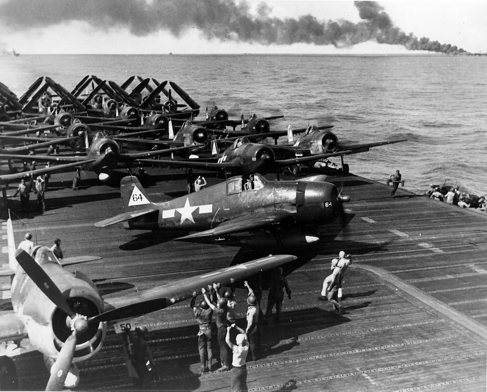 Grumman F6F-5 Hellcats on teh flight deck of USS Enterprise (CV-6), 30 october 1944. The aircraft carrier USS belleau Wood (CVL-24) is burning on the horizon, after being struck by a kamikaze. (U.S. navy)