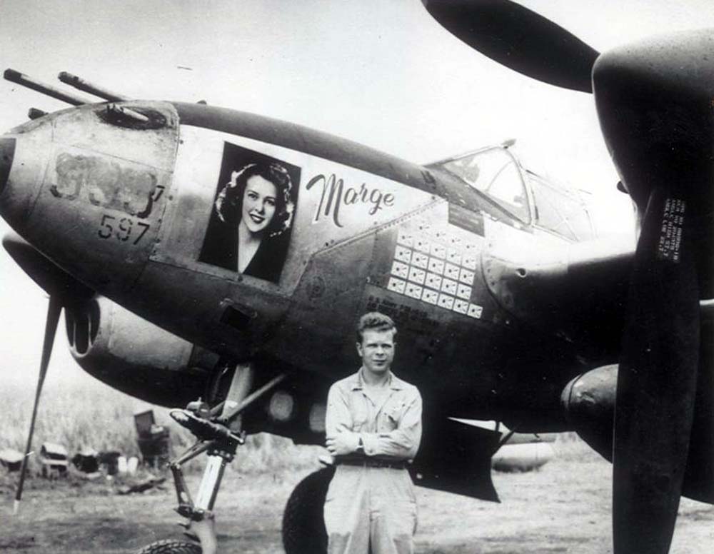 Dick Bong poses with "Marge," his Lockheed P-38J Lightning. A large photograph of his fiancee, Miss Marjorie Vattendahl, is glued to the fighter's nose.